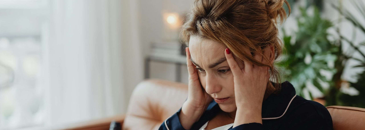 Femme assise au bord de son lit se tenant la tête au réveil, souffrant d'un mal de tête matinal